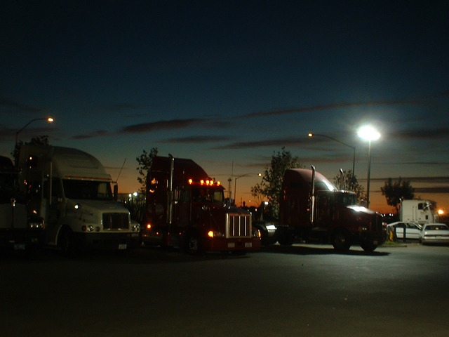 nákladní automobily v řadě, tři stojí v řadě vedle sebe, je tma, svítí pouliční lampa